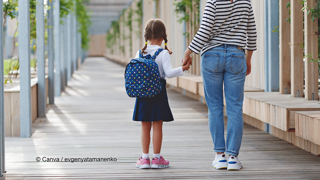 Auf dem Schulweg: Ein Mädchen mit Rucksack auf dem Rücken hält die Hand einer erwachsenen Person. Auf dem Weg zur Schule vor der Arbeit ist ein Unfall kein Wegeunfall.