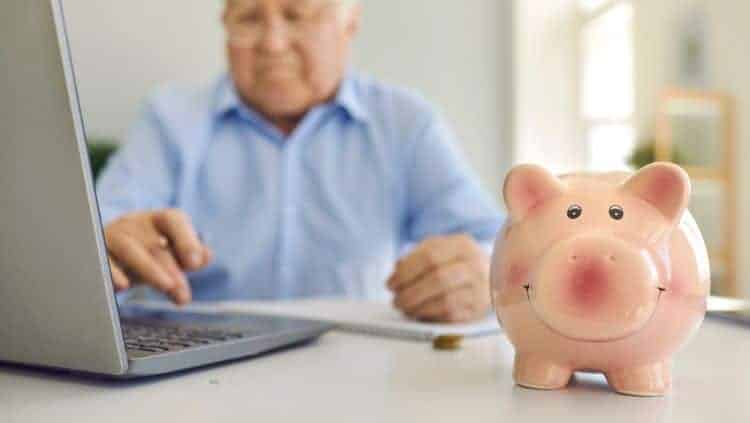 Rentner am PC und Sparschwein auf Tisch