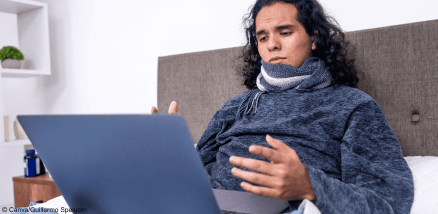 Eine Person, die die Online-Krankschreibung im Bett über den Laptop ausfüllt.